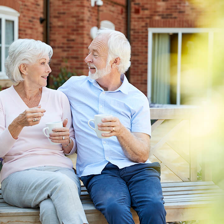 Retired Couple Sitting On Bench With Hot Drink In Retirement home